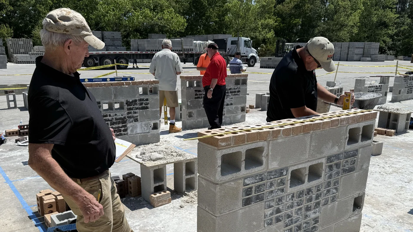 Participants checking a practice masonry wall with a level and clipboard.