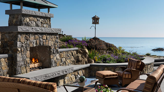 The outdoor fireplace and patio are made from natural stone. Natural stone copings cover the stone walls, and natural stone slabs were used for the hearth.